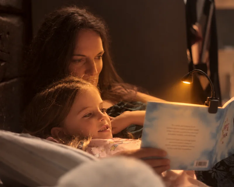 A mother and child reading The Sleep & Dream Book together by a warm amber clip light